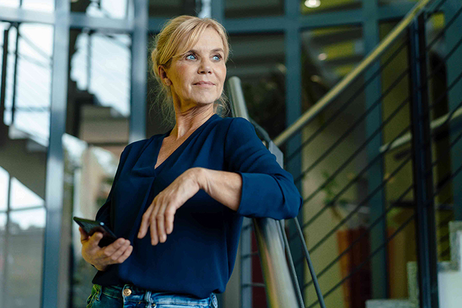 Frau lehnt sich an ein Treppengeländer, während sie entspannt und nachdenklich in die Ferne schaut.