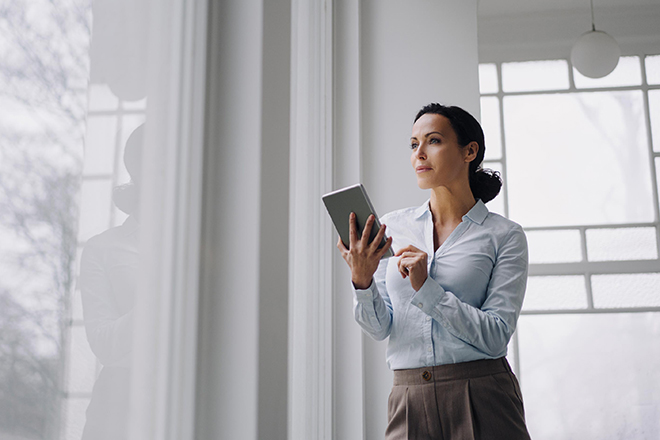 Eine Frau hält ein Tablet in der Hand und schaut gebannt aus dem Fenster.