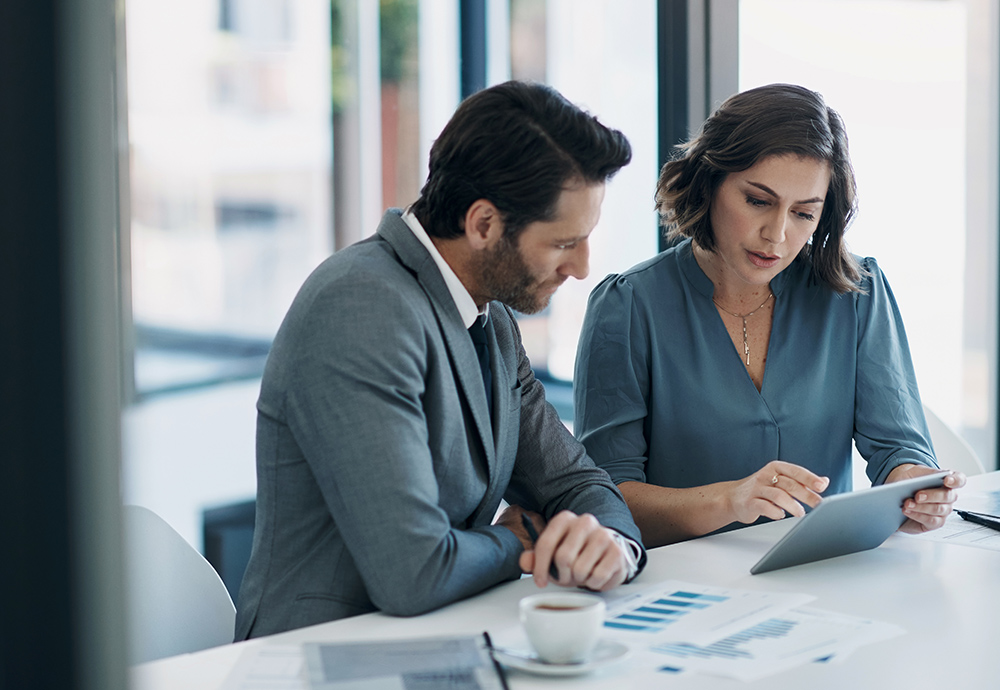 Mann und Frau in schicker Kleidung sitzen an einem Tisch und sprechen im Büro über Investor Relations.