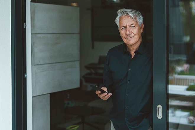 Ein Mann im Hemd steht im Glas-Türrahmen und hält sein Handy in der Hand