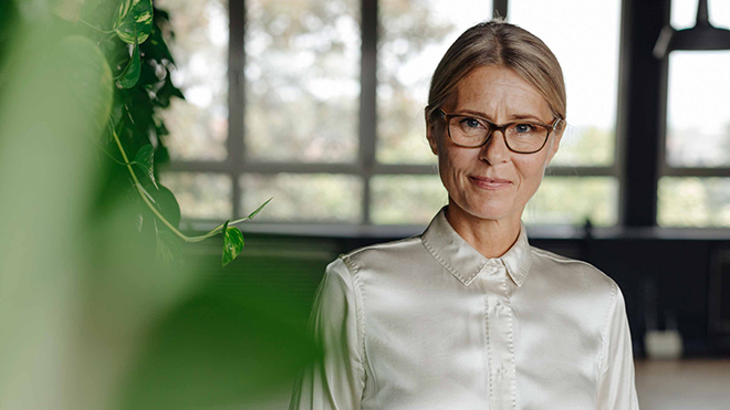 Frau mittleren Alters mit Brille schaut zielgerichtet in die Kamera.