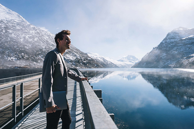 Ein Mann steht an einem Steg vor einem See, umgeben von vereisten Bergen.